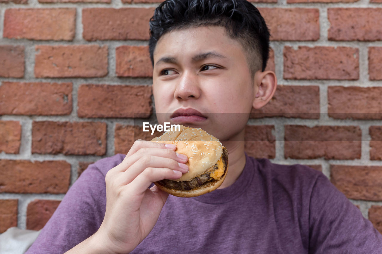 Boy making a bored face eating a hamburger.