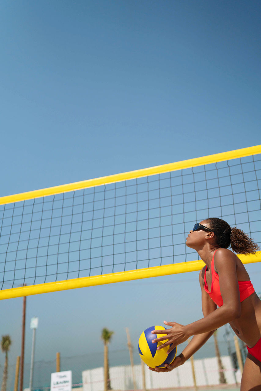 sports, adult, volleyball, young adult, one person, women, lifestyles, net sports, clothing, sky, leisure activity, clear sky, copy space, ball game, sports equipment, day, ball, nature, exercising, three quarter length, athlete, blue, sunlight, sports clothing, sunny, outdoors, beach volleyball, net - sports equipment, side view, holding, player, tennis, motion, relaxation, low angle view, standing, hairstyle, full length