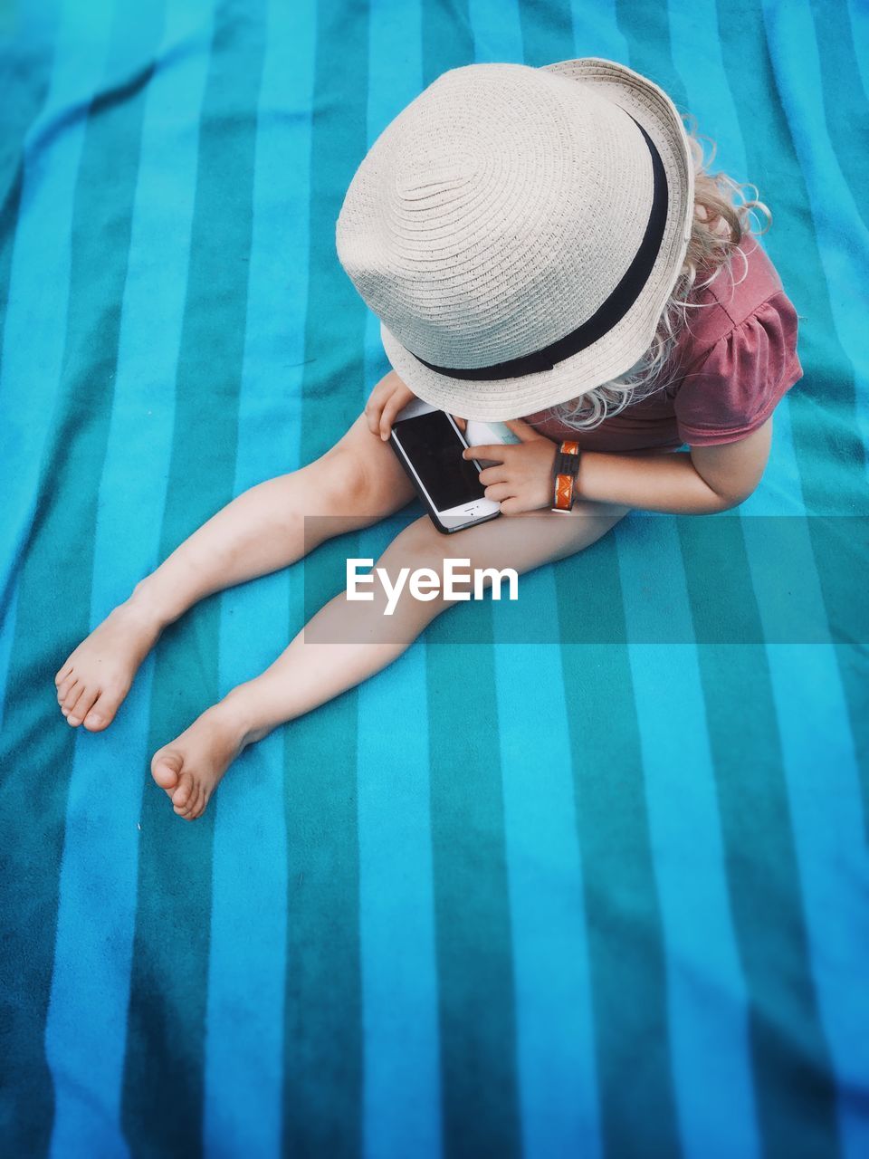 High angle full length of girl wearing sunhat while using smart phone on beach towel