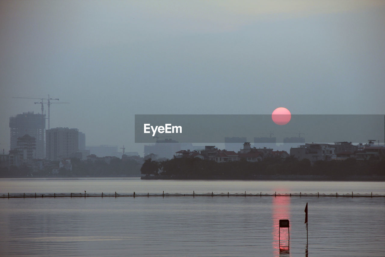 SCENIC VIEW OF LAKE BY CITY BUILDINGS AGAINST SKY