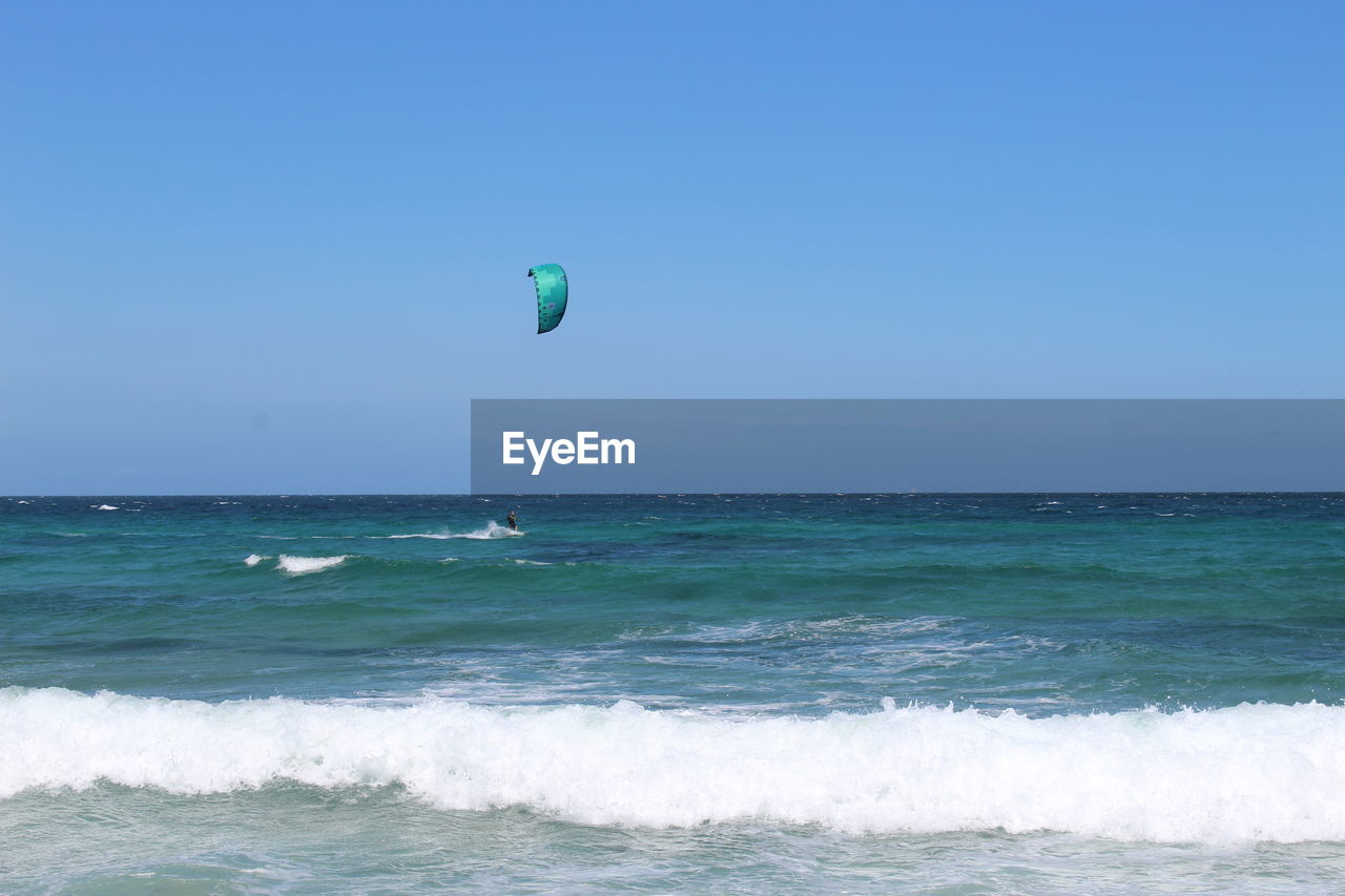 Scenic view of sea against clear blue sky with person kiteboarding in background