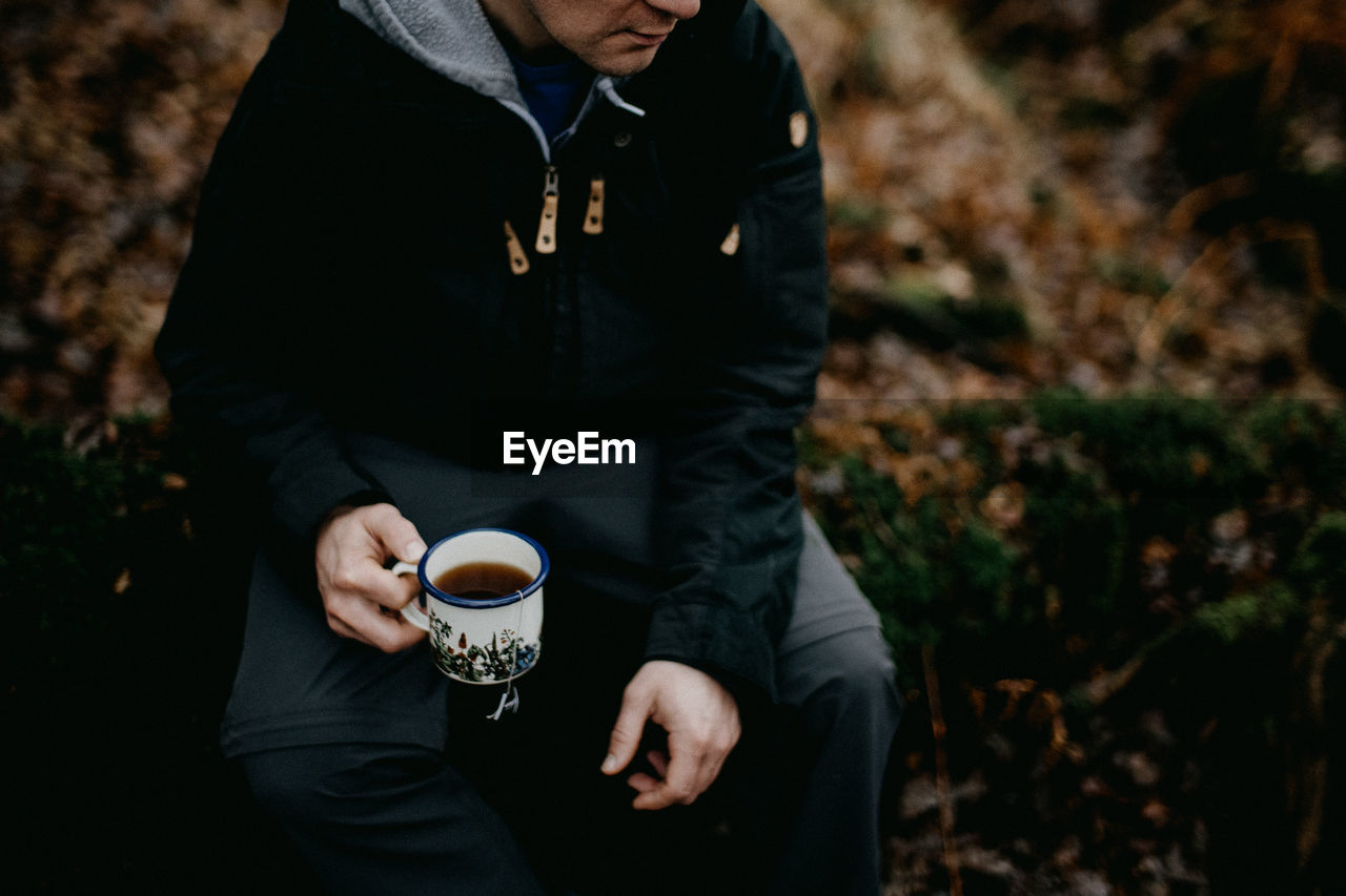 midsection of man holding coffee while sitting on field