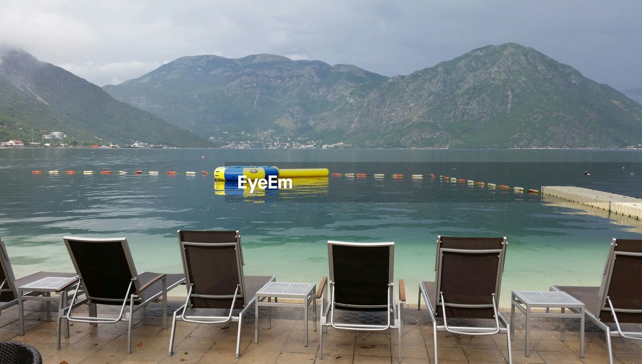 Lounge chairs by river and mountains against sky