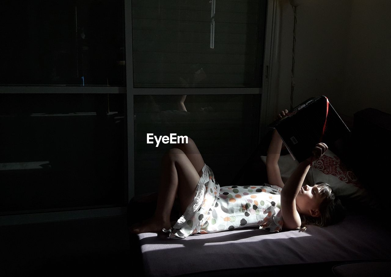 Girl reading book while lying on bed at home