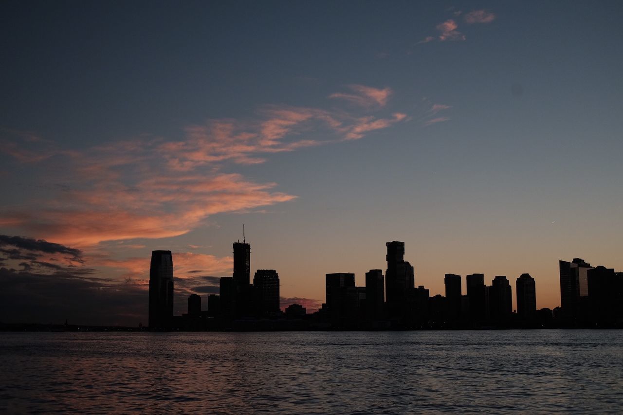 SILHOUETTE BUILDINGS BY SEA AGAINST SUNSET SKY