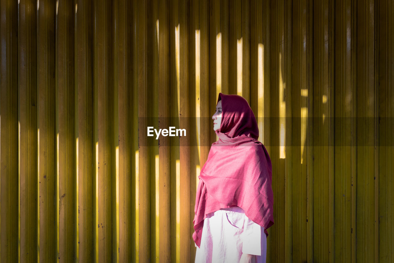 Woman wearing headscarf while standing against yellow corrugated iron