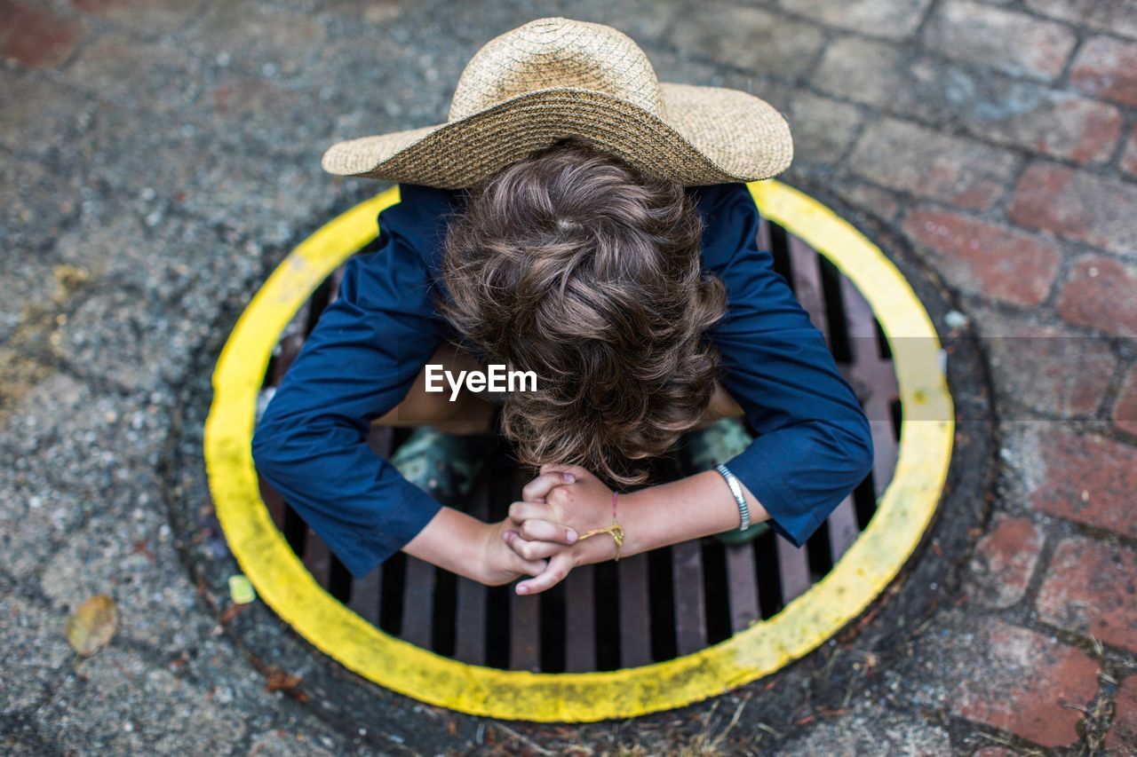 High angle view of boy wearing hat while crouching on manhole