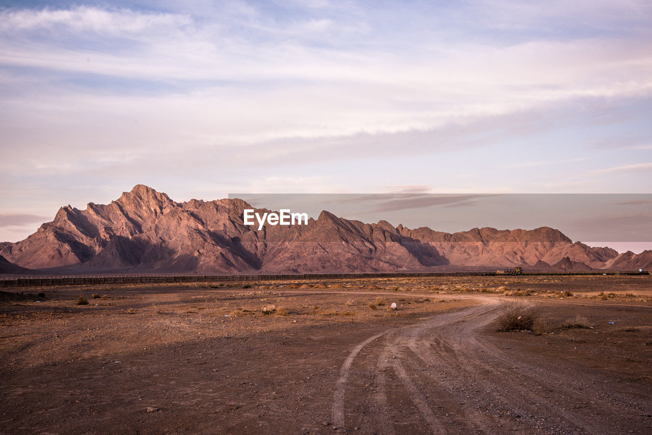 Scenic view of field with round directing going to the mountain against sky