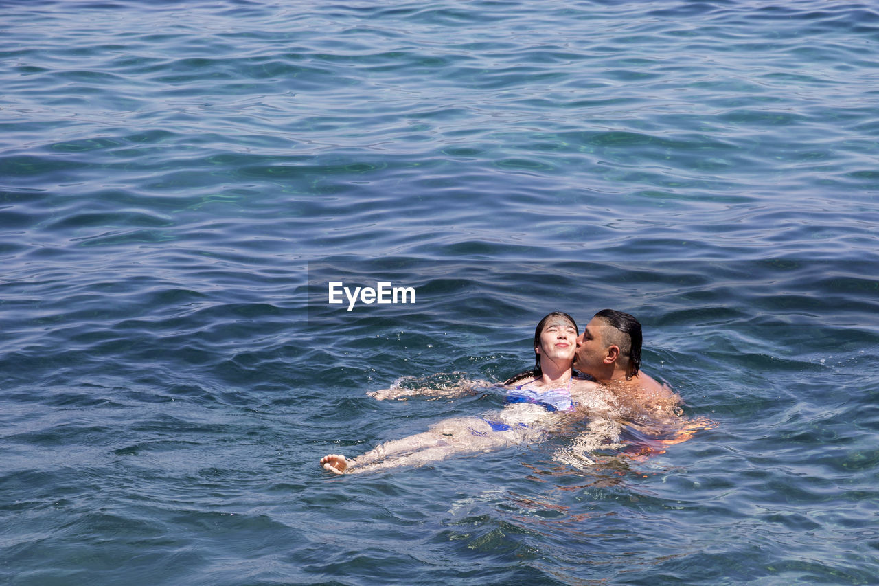 Shirtless man kissing woman in sea
