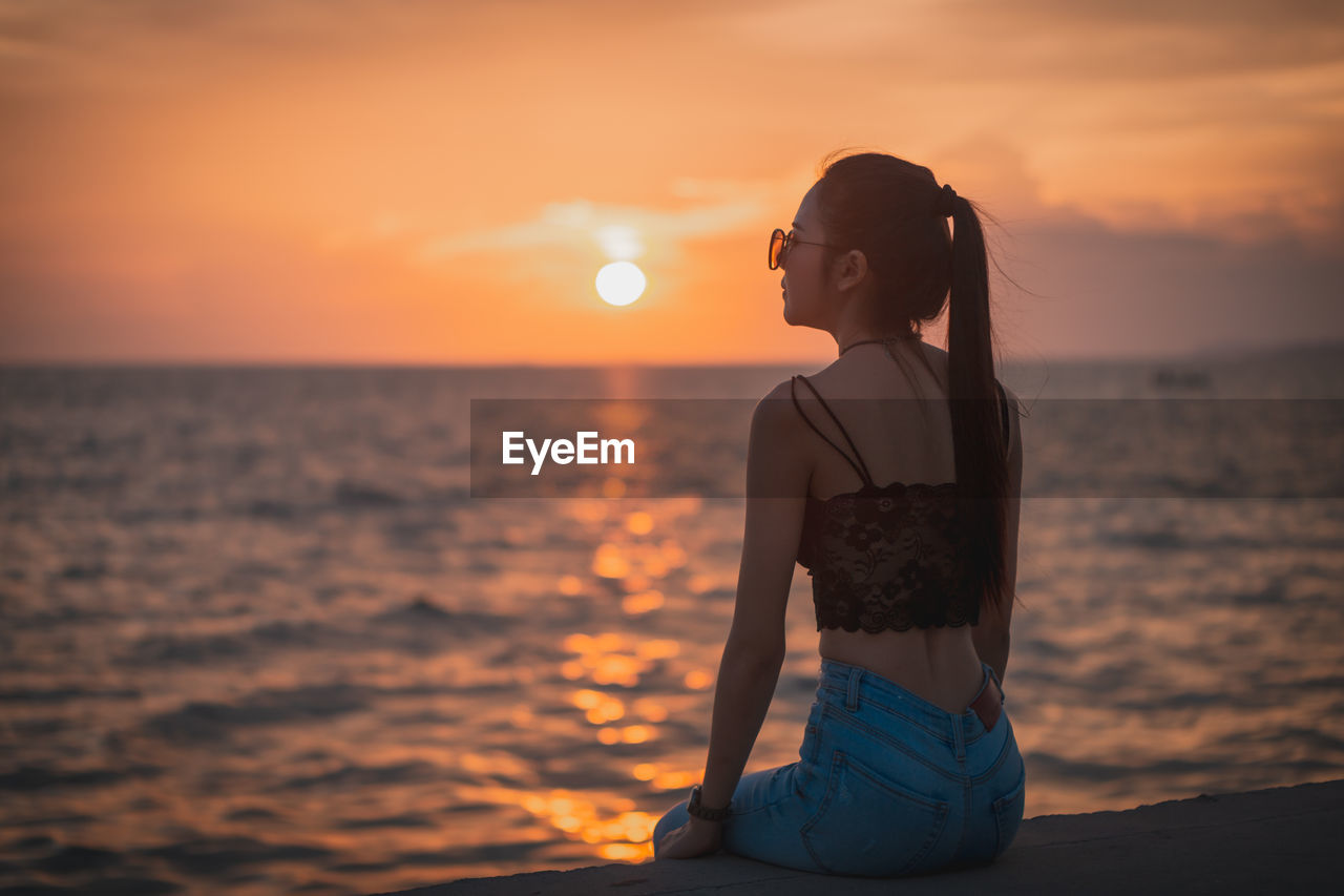 WOMAN LOOKING AT SEA AGAINST ORANGE SKY