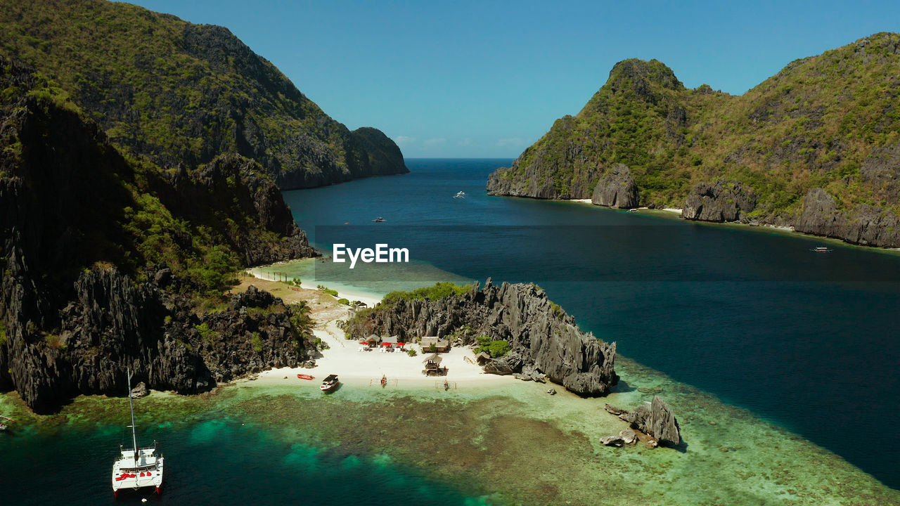 Tropical landscape bay with beach and clear blue water surrounded by cliffs, aerial drone. 