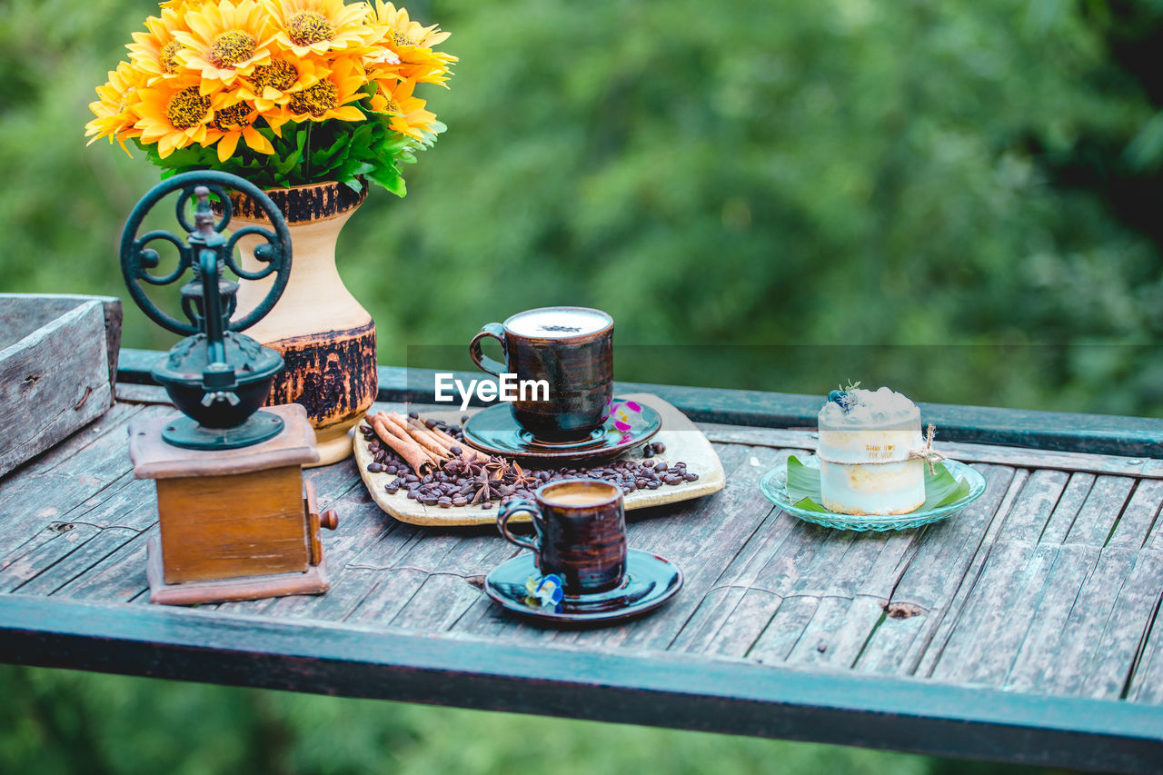flower, flowering plant, plant, nature, table, wood, no people, freshness, food and drink, beauty in nature, vase, green, day, outdoors, cup, food, mug, yellow, focus on foreground, container