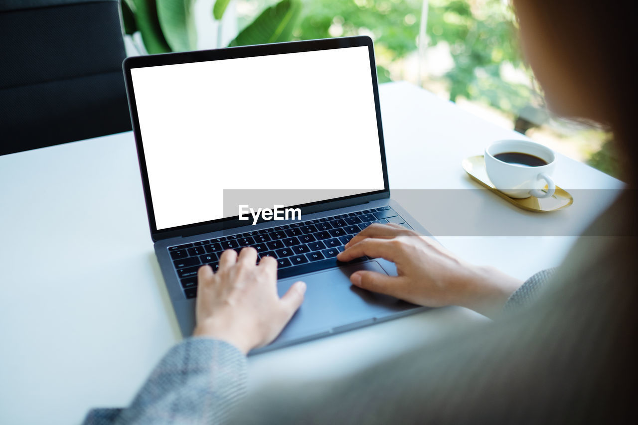 cropped hands of woman using laptop on table