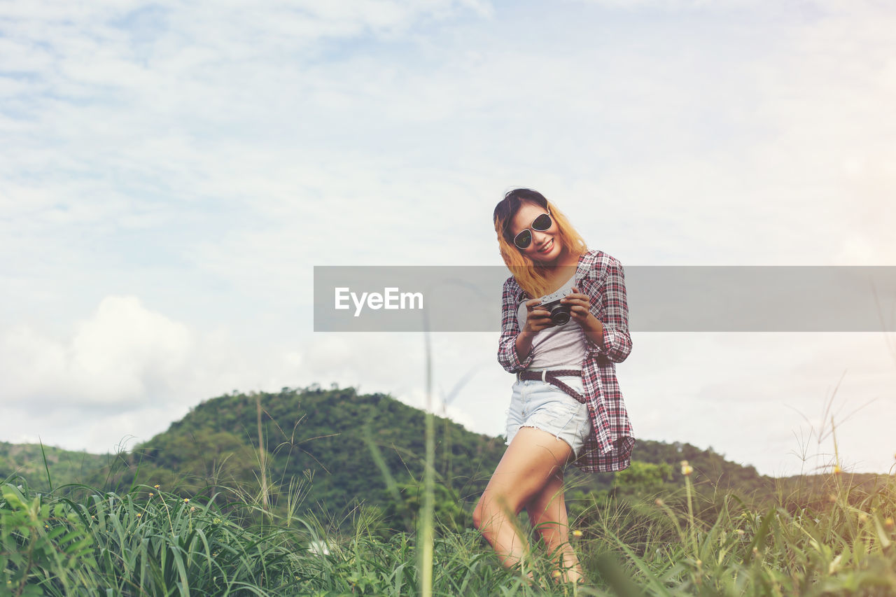 Portrait of smiling young woman standing on field against sky