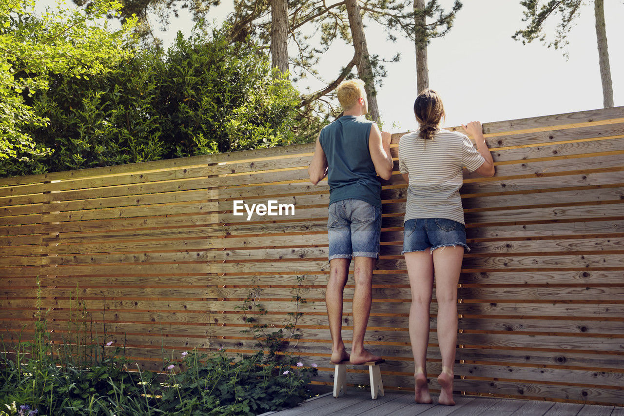 Young couple looking over wooden fence at back yard