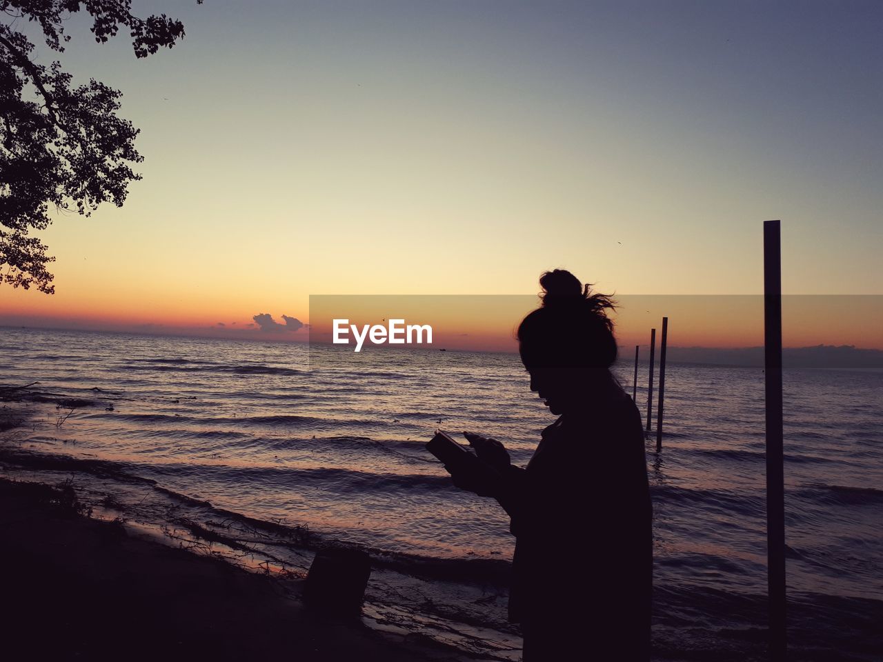 Silhouette woman standing at beach against sky during sunset