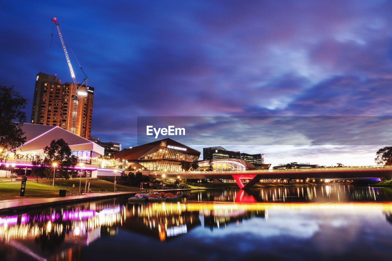 Illuminated buildings by river against sky at night