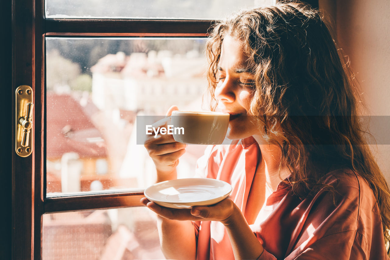 Beautiful woman drinking coffee near the window at cafe with amazing view.