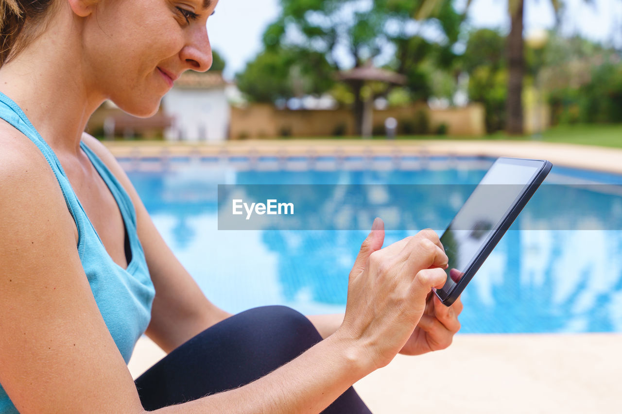 Horizontal side view of woman connecting with technology to a gym class next to a swimming pool.