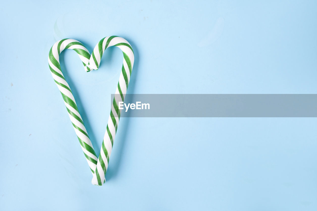 Green and white candy cane in the shape of heart on the blue background.