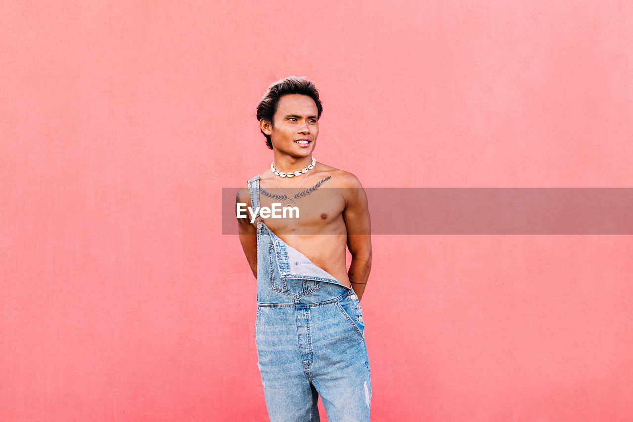 Gay man standing against pink background