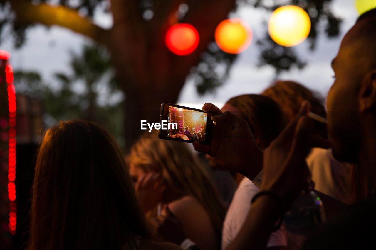 REAR VIEW OF WOMAN PHOTOGRAPHING WITH MOBILE PHONE AT CAMERA