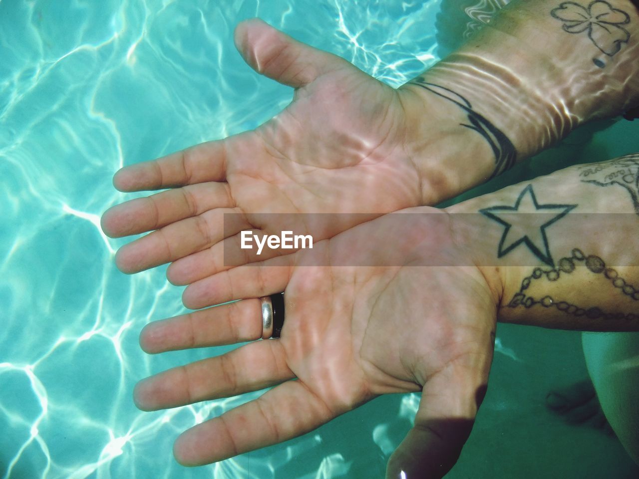 High angle view of cropped tattooed hands in swimming pool