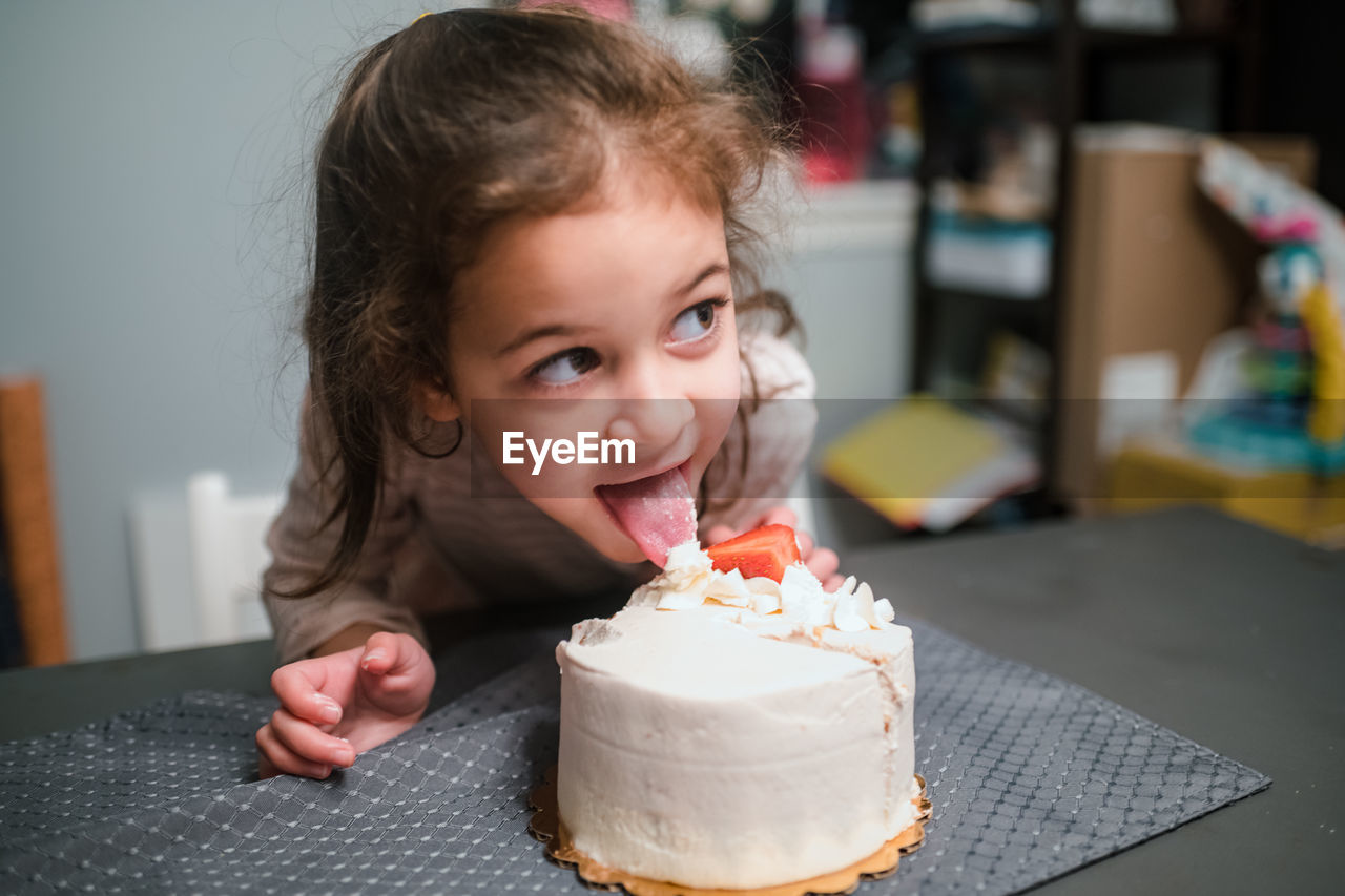 Preschool age girl licking birthday cake and looking off camera