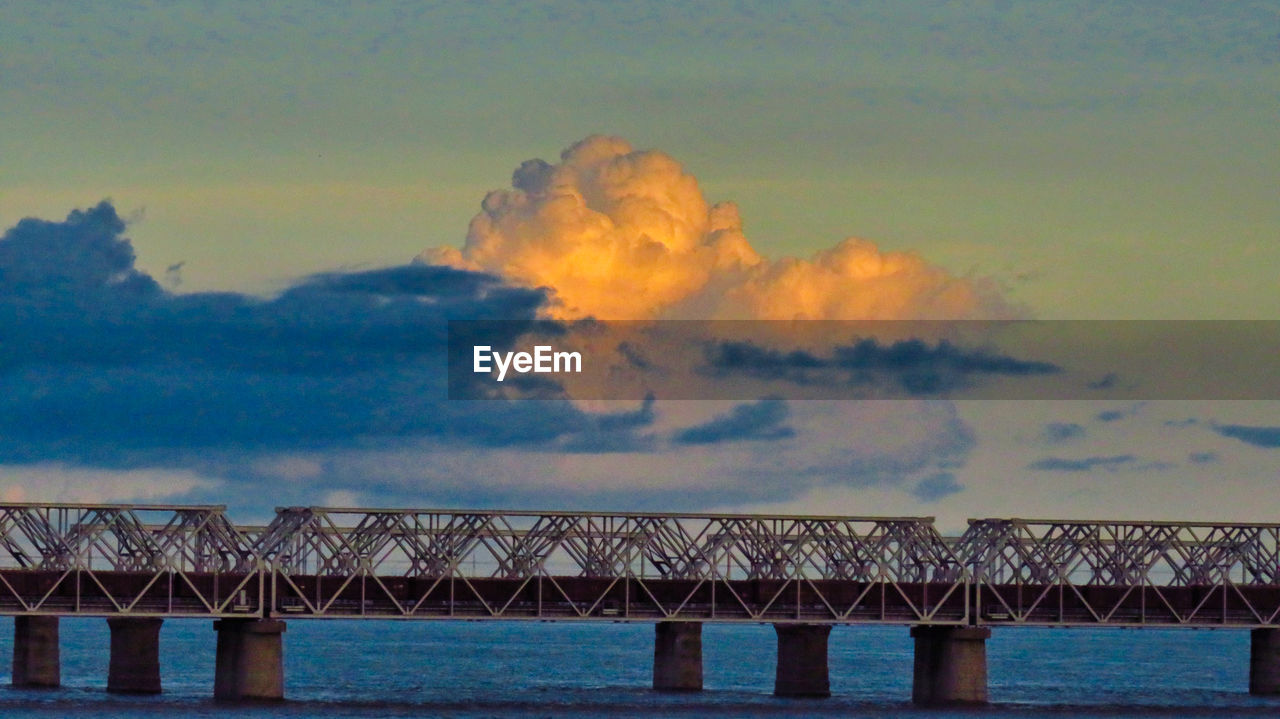 LOW ANGLE VIEW OF BRIDGE OVER SEA AGAINST SKY AT SUNSET
