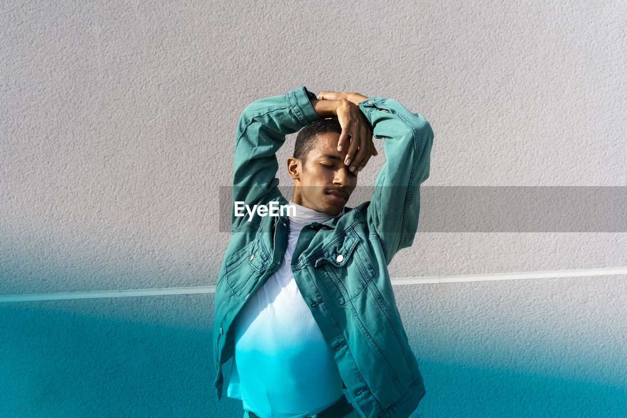 Man with eyes closed dancing while standing against multi colored wall