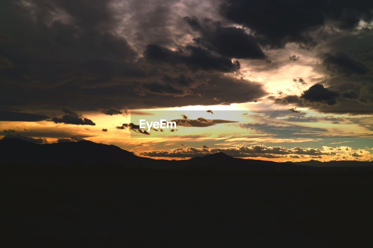 Silhouette of mountain against cloudy sky at sunset