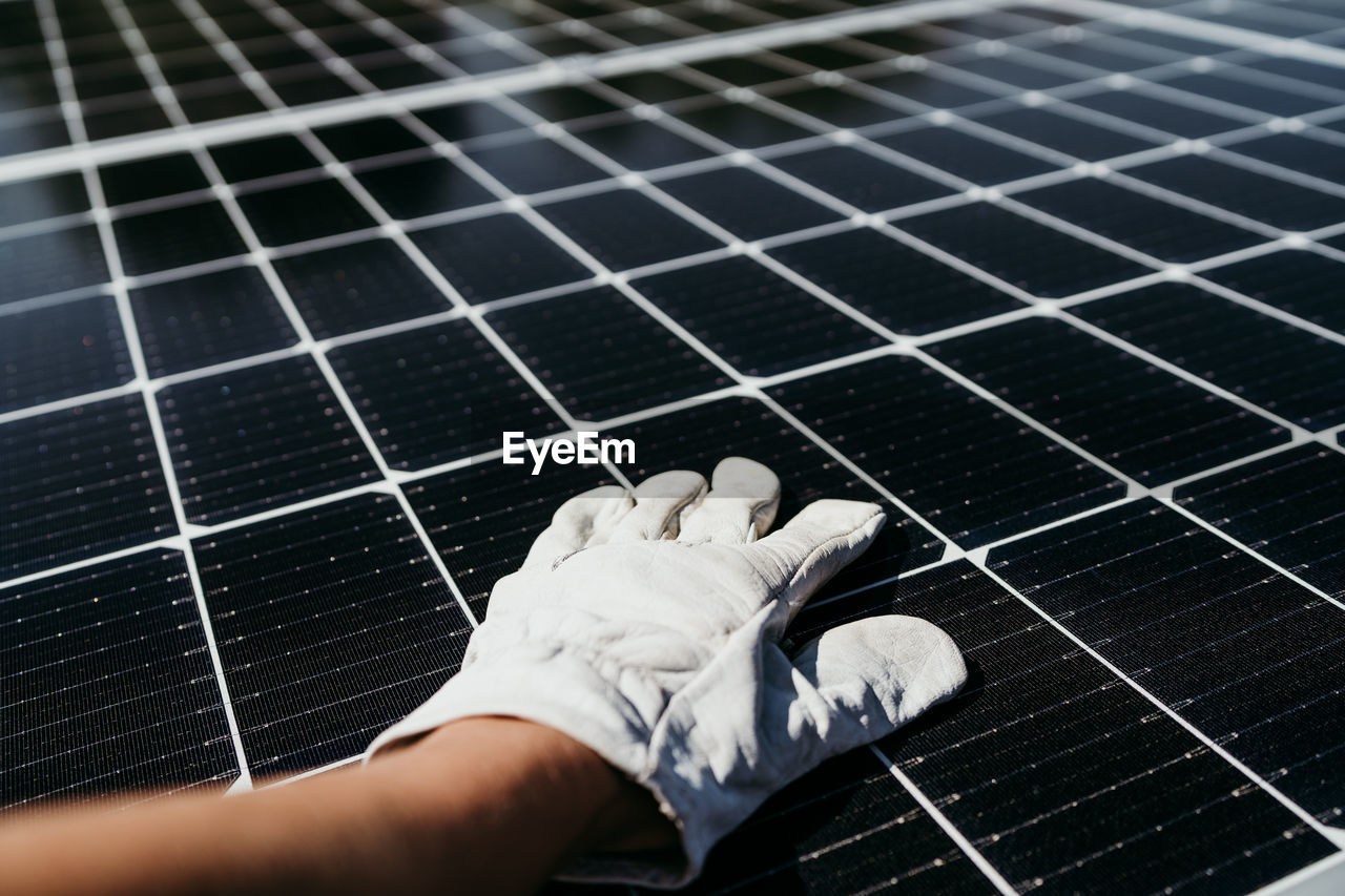 Hand of mature technician man touching solar panels on house roof for self consumption energy