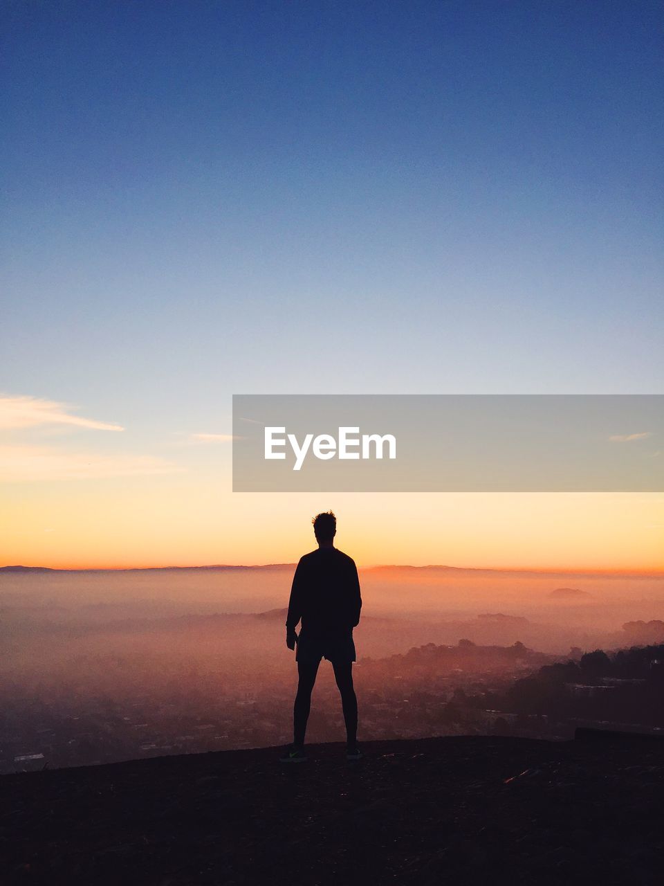 Rear view of silhouette man standing on mountain against sky