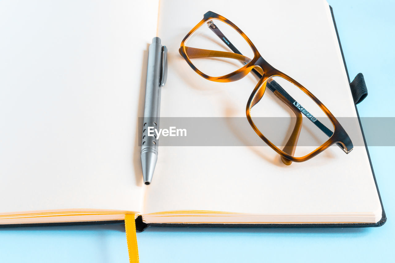 High angle view of eyeglasses with pen on blank diary against blue background