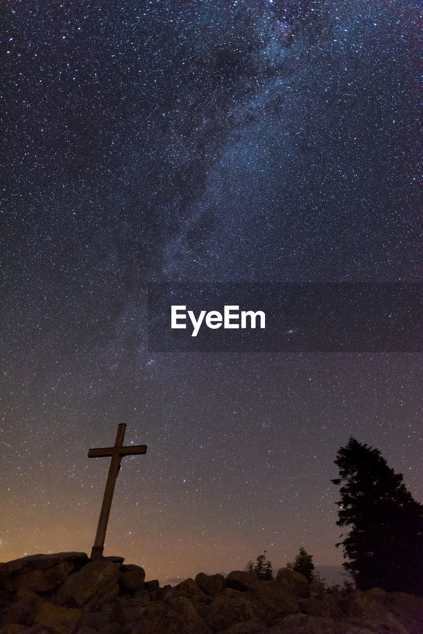 LOW ANGLE VIEW OF CROSS ON TREE AGAINST STAR FIELD