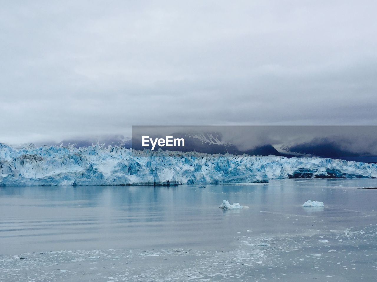 Scenic view of sea by ice mountain against cloudy sky