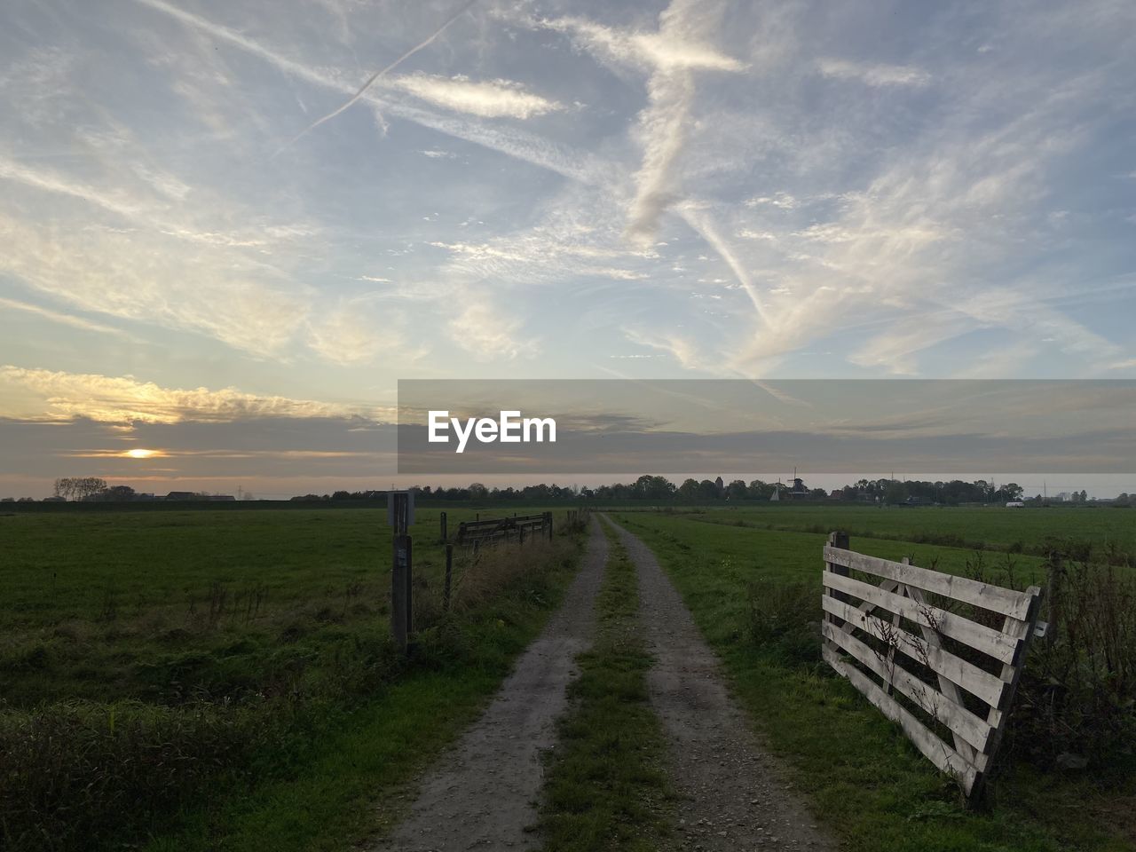 Road amidst field against sky during sunset