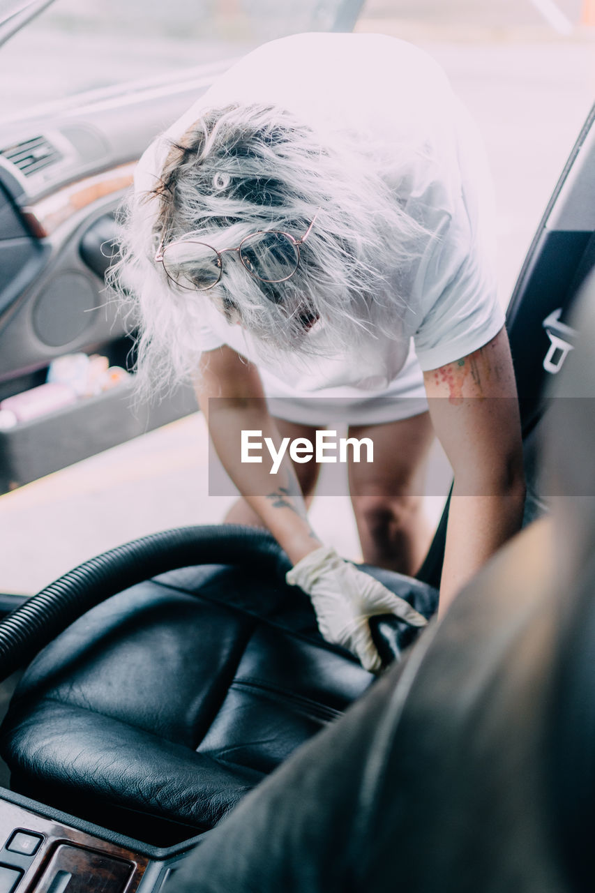 Vacuuming the interior of a passenger car using an industrial vacuum cleaner. woman works in protective medical mask. protection against coronavirus