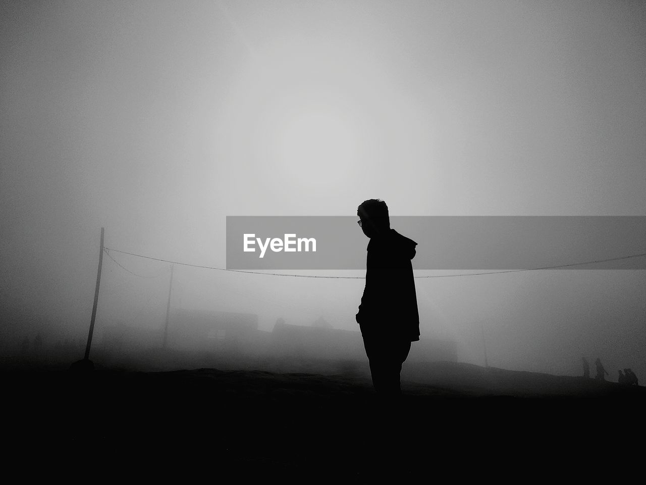 Silhouette man standing on field against sky during foggy weather