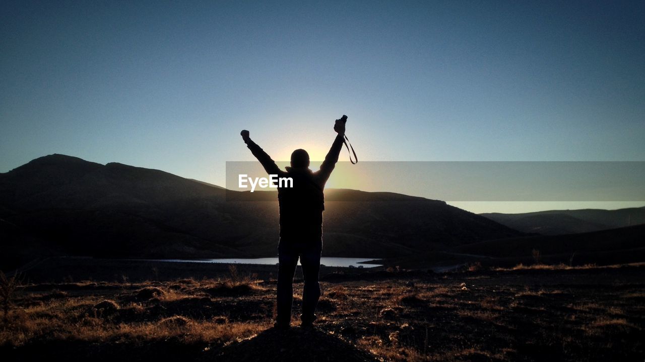 Silhouette photographer with arms raised standing on field against clear sky