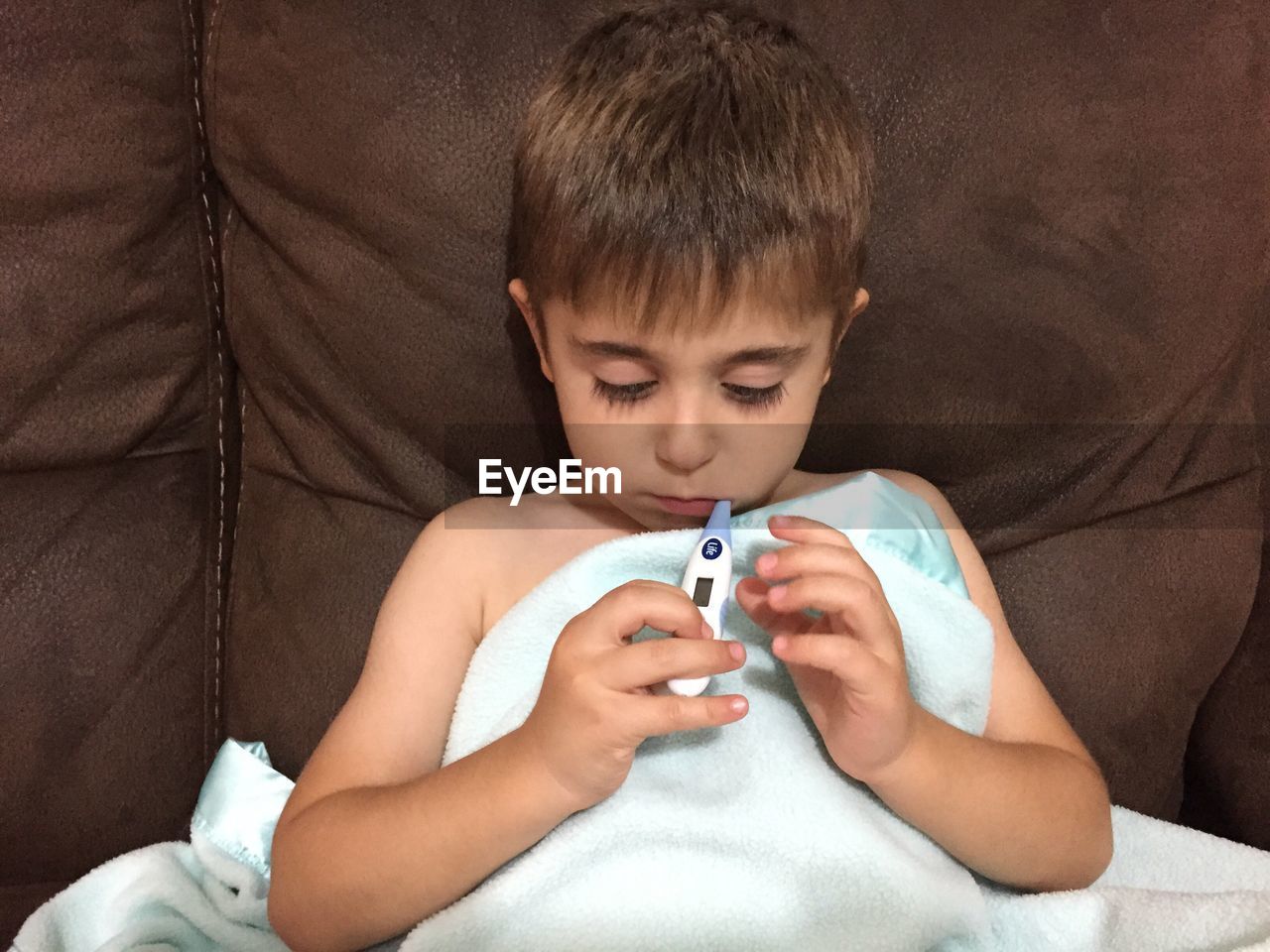 Boy using thermometer on sofa at home