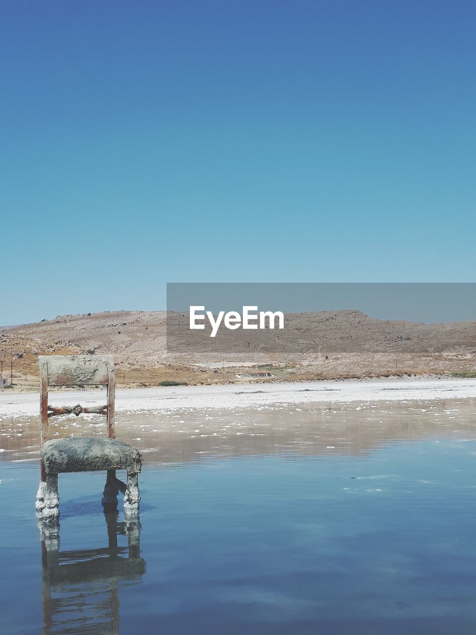 Abandoned chair in salt lake against clear blue sky 