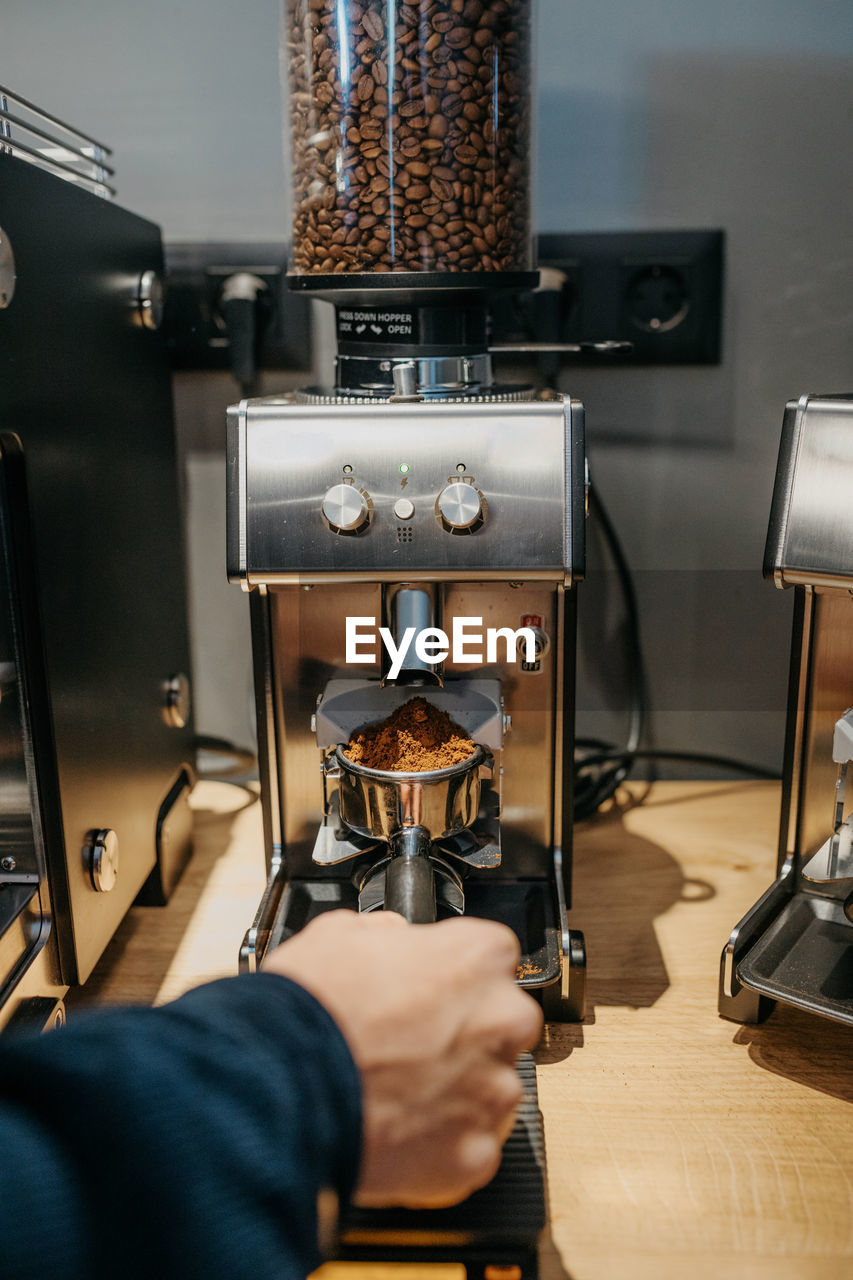 Crop unrecognizable barista using coffee grinder while preparing aromatic fresh coffee in cafe in daytime