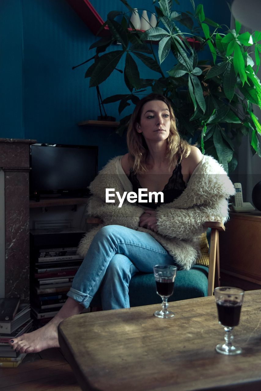 Young woman looking away while sitting on chair at home