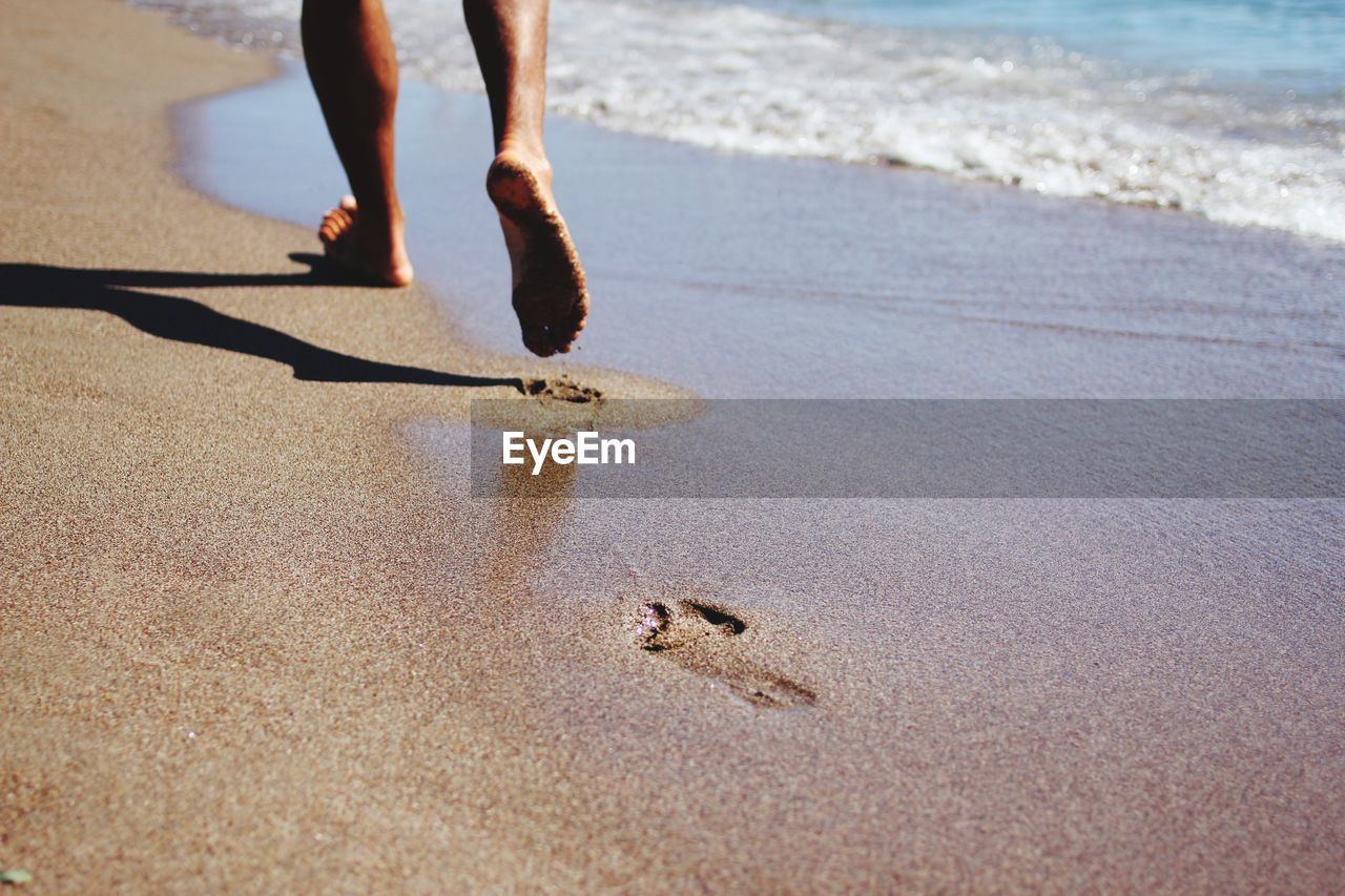 Low section of person walking on shore at beach during sunny day