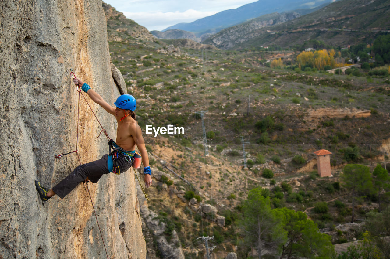 Shirtless man rock climbing against landscape