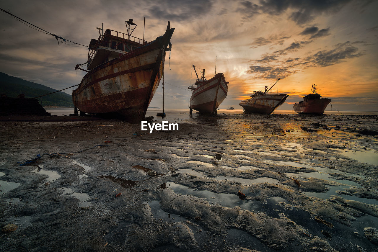 Nautical vessel on beach against sky during sunset