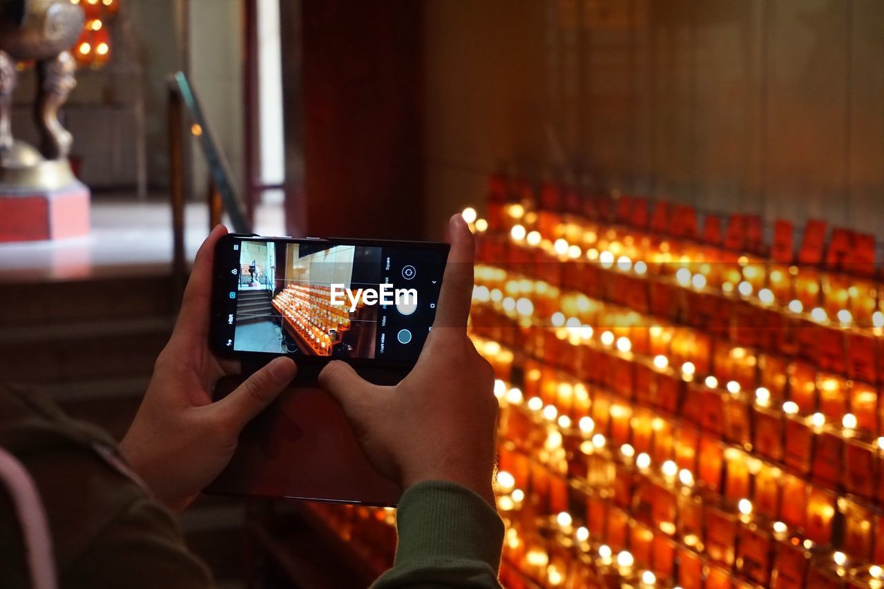 Close-up of human hands photographing illuminated candles with mobile phone