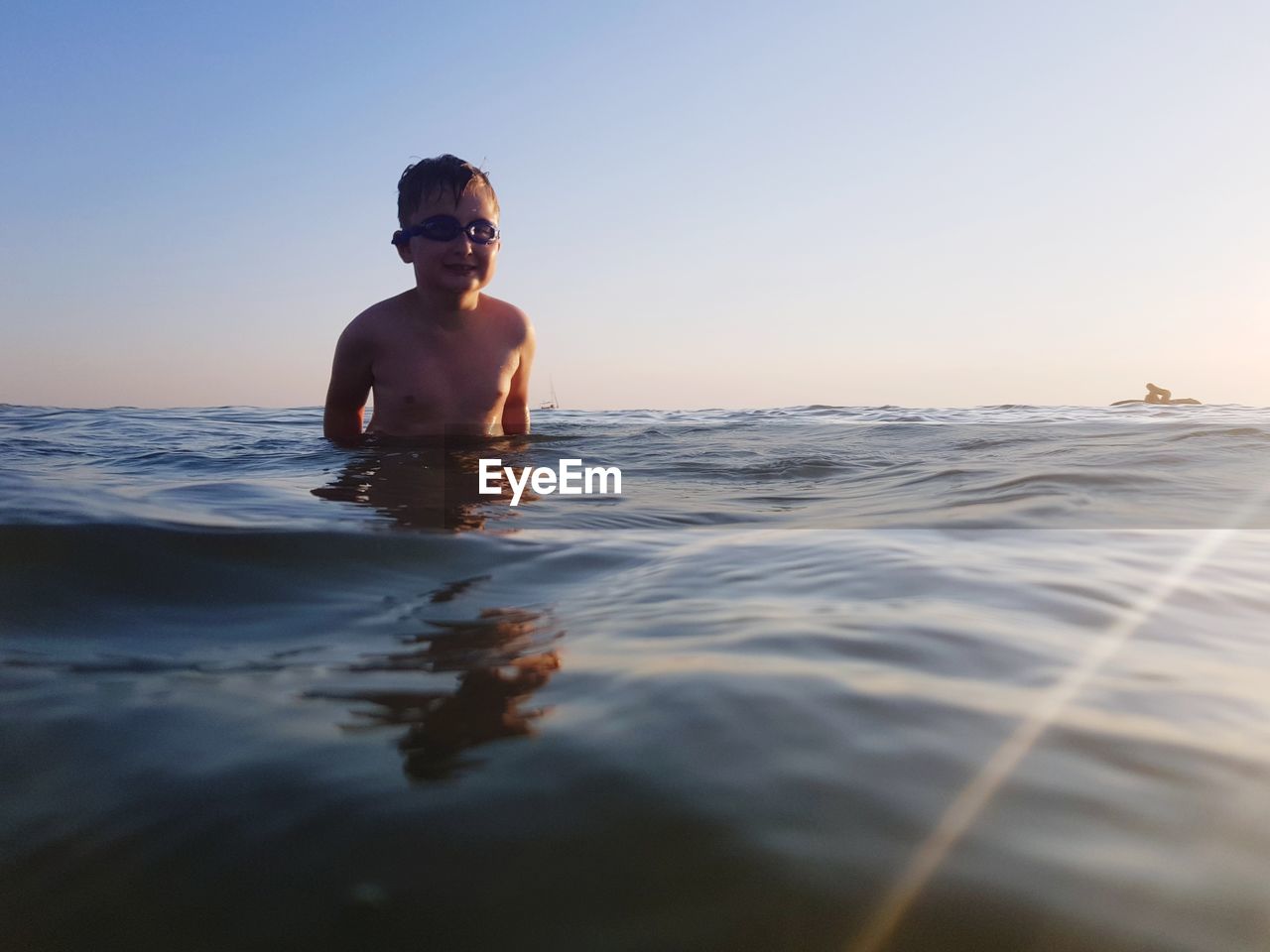 Portrait of shirtless boy in sea against clear sky during sunset