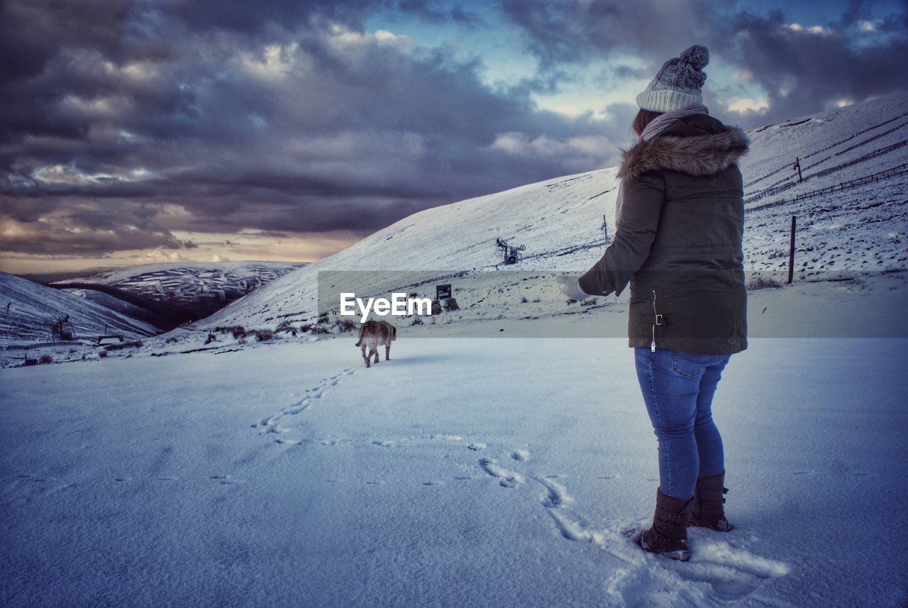 Woman standing on snowy field against cloudy sky during sunset